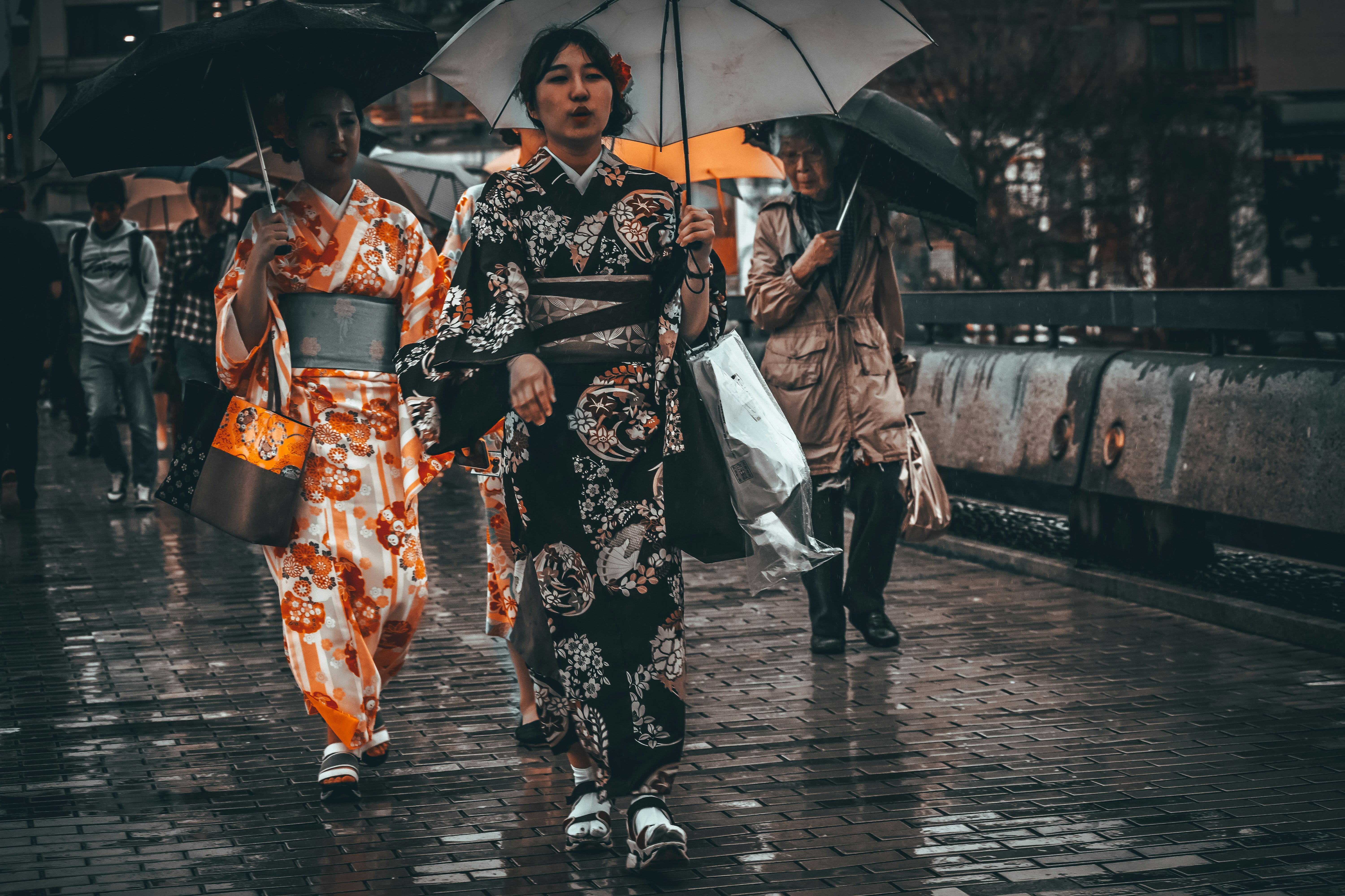 2 women in black and white kimono holding umbrella walking on sidewalk during daytime